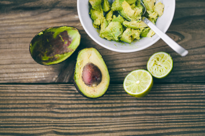 A high-angle view of Guacamole being prepared with avocados and lime on a wood grain background